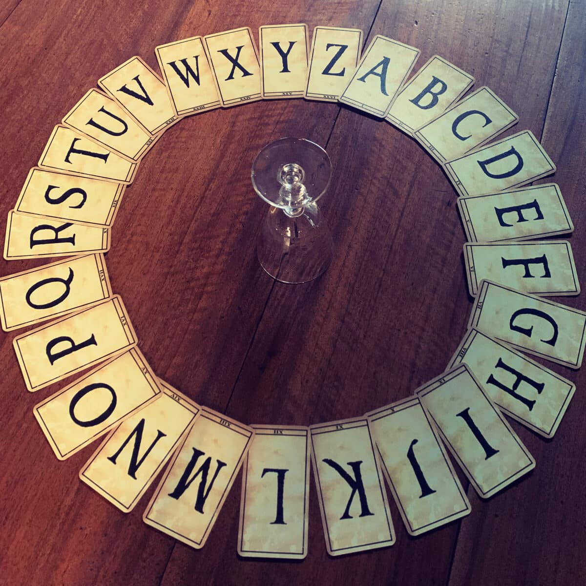 Cartes de l'alphabet disposées en cercle autour d'un verre pour une séance de spiritisme, Soirées de l'Étrange à Reims