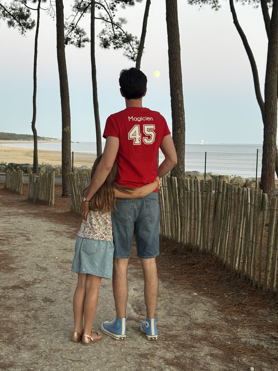 Cyril Regard de dos, en t-shirt rouge de magicien du Club Med, avec sa fille face à la plage de La Palmyre