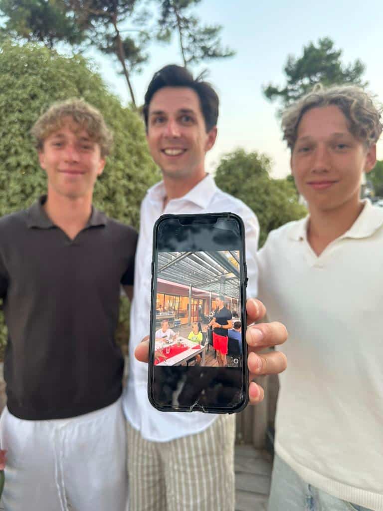 Cyril Regard entouré des deux frères qu'il avait vus enfants quatre ans plus tôt au Club Med de La Palmyre, montrant la photo d'époque sur un téléphone