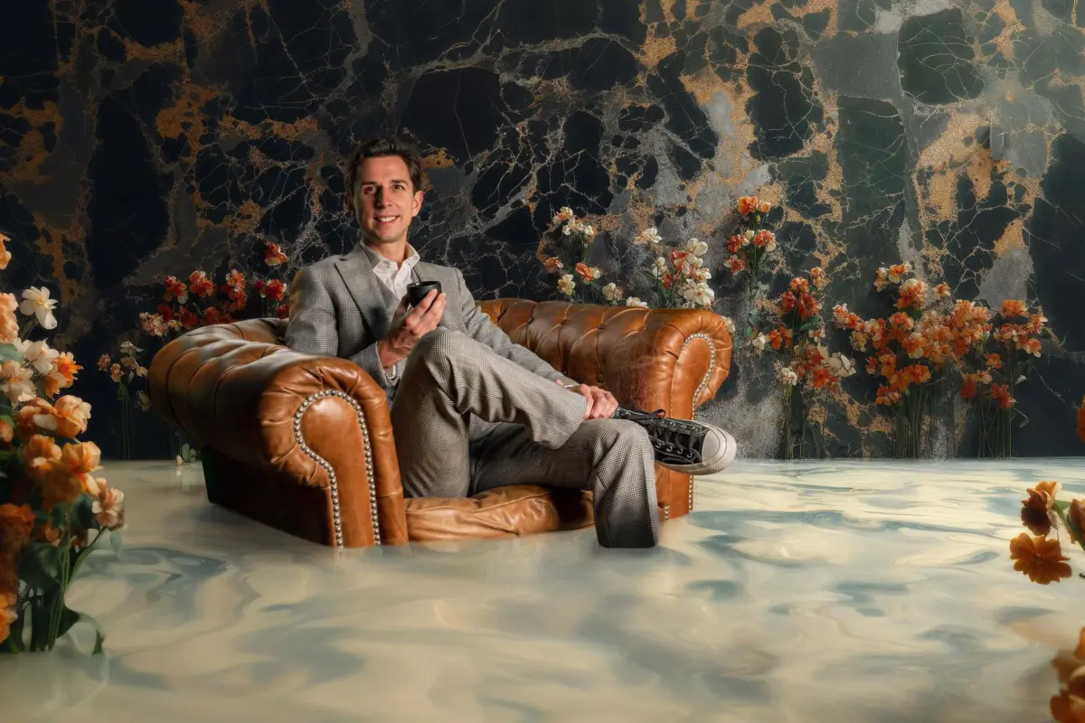Cyril Regard dans un fauteuil Chesterfield, une tasse à la main, entouré de fleurs